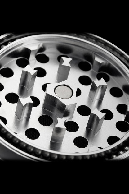 Close-up of a metal cannabis grinder with visible teeth and chambers.