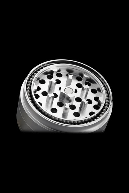 Silver cannabis grinder with visible grinding teeth and collection chamber, isolated on black.