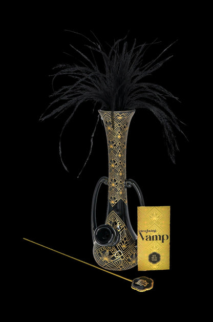 Art Deco-inspired cannabis water pipe with black feather plume, presented with branded packaging on a dark background.