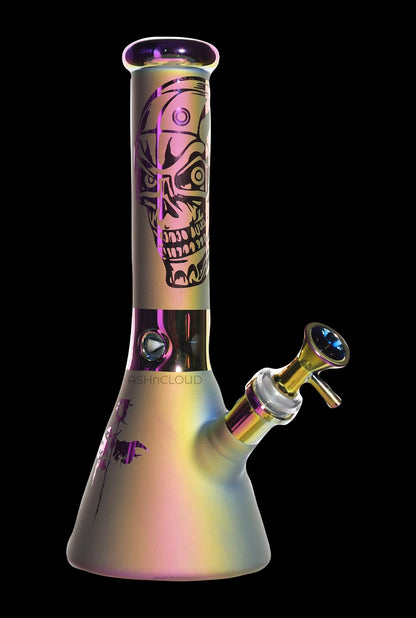 Angled front view of the Smoke Cartel Electro Plated Beaker Bong - 10 in., showing its iridescent finish, skull graphic on the neck, and tilted bowl against a black background