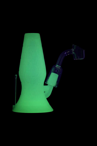 Glowing green glass dab rig with purple quartz insert, isolated on black.
