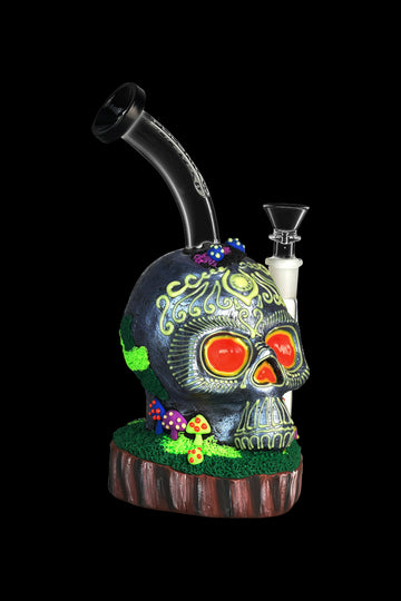 Intricately detailed glass skull water pipe with glowing red eyes and colorful mushroom accents, displayed on a wooden base. - Pulsar Voodoo Skull Water Pipe