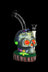 Intricately detailed glass skull water pipe with glowing red eyes and colorful mushroom accents, displayed on a wooden base. - Pulsar Voodoo Skull Water Pipe
