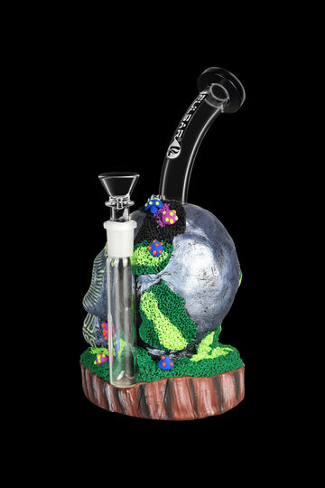 A colorful, sculpted glass water pipe resembling a miniature forest scene with mushrooms and moss, featuring a clear glass bowl and stem. - Pulsar Voodoo Skull Water Pipe
