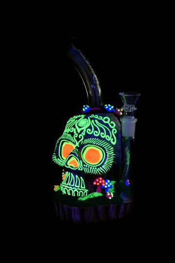 Glowing glass water pipe shaped like a skull, illuminated under blacklight. - Pulsar Voodoo Skull Water Pipe