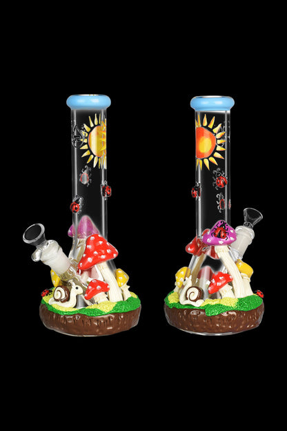 Two glass bongs decorated with a whimsical mushroom and forest scene, featuring colorful mushrooms, a winding path, and a sun design on a black background.