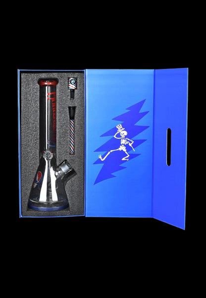 A glass water pipe (bong) with red accents inside a black display case, next to a blue box featuring a dancing skeleton graphic, likely related to cannabis use.
