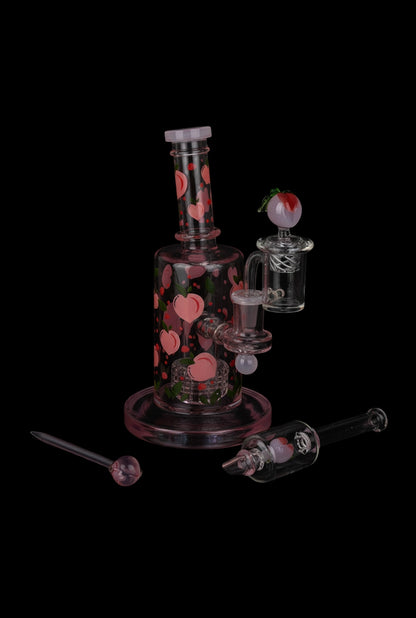 Angled front view of the Pulsar Fruit Series Peaches & Cream Glow in The Dark Dab Rig Kit showing pink peach motifs on clear glass.