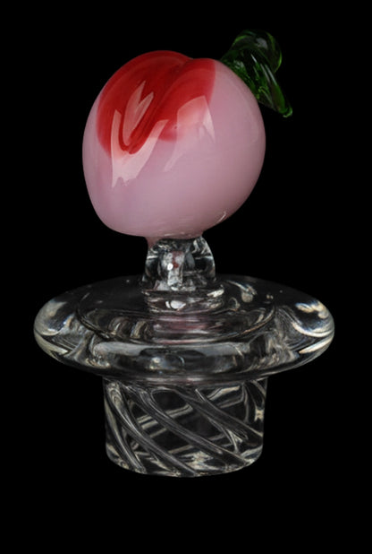 Close-up front view of the Pulsar Fruit Series Peaches & Cream Glow in The Dark Dab Rig Kit - 8" / 14mm F, showing a glossy pink-and-red peach topper with a green leaf on a clear swirled glass joint against a black background