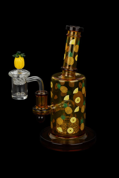 Angled close-up of the 8" Pulsar Fruit Series Pineapple Express Glow In The Dark Dab Rig Kit - 8" / 14mm F showing amber glass decorated with pineapples against a black background