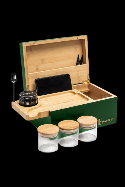 A green wooden cannabis storage box containing a smartphone, grinder, jars, and smoking tools on a black background.