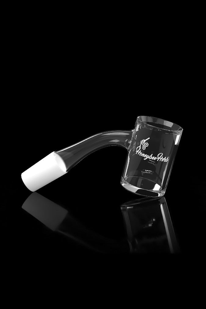 Clear glass dab rig with a bent neck and branded with “Honeybee Herb” logo, reflected on a glossy black surface.