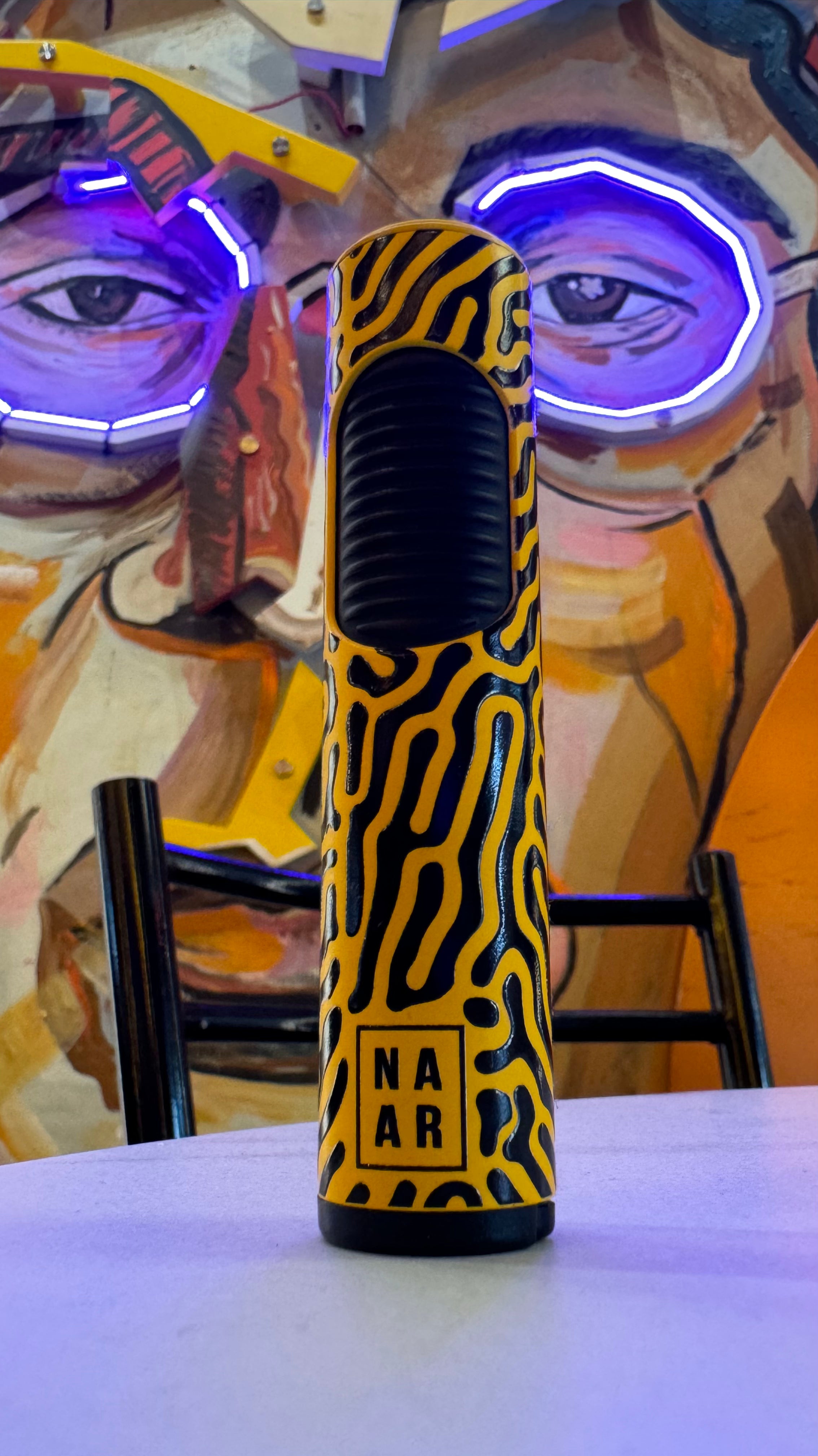 A patterned black and yellow cannabis oil vape cartridge with “NAR” printed on its side, displayed against a vibrant, colorful portrait background.