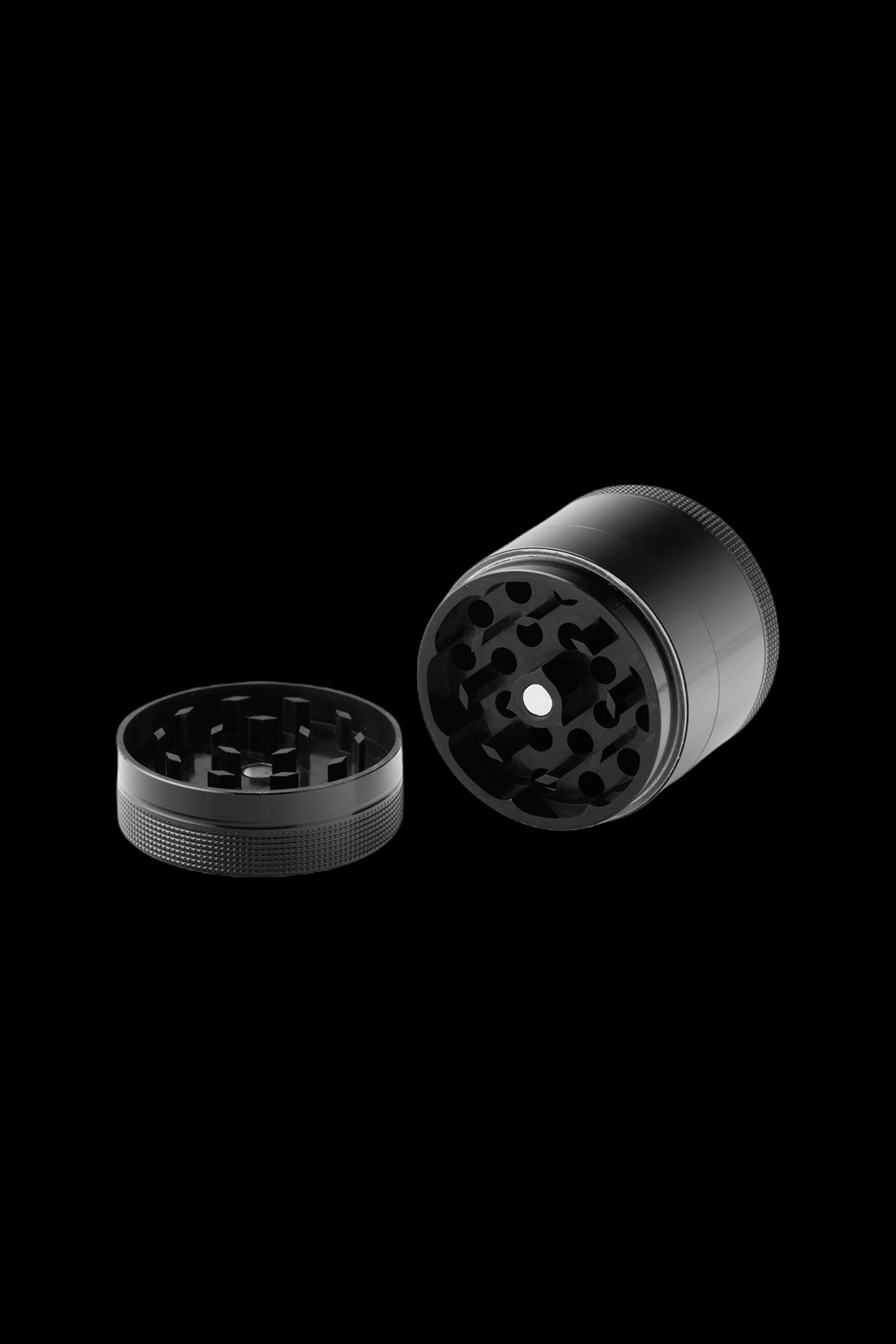 Black metal cannabis grinder, disassembled into two sections, on a black background.