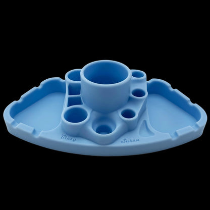 Front-facing view of a light blue Blazy Susan Deluxe Dab Station with central cup and multiple circular and rectangular wells on a scalloped tray against a black background