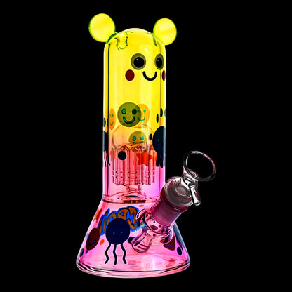 Three-quarter view of the Croia Glass Cute Character Beaker Bong with Jellyfish Design showing its yellow-to-pink gradient glass, smiling faces and jellyfish motifs against a black background.