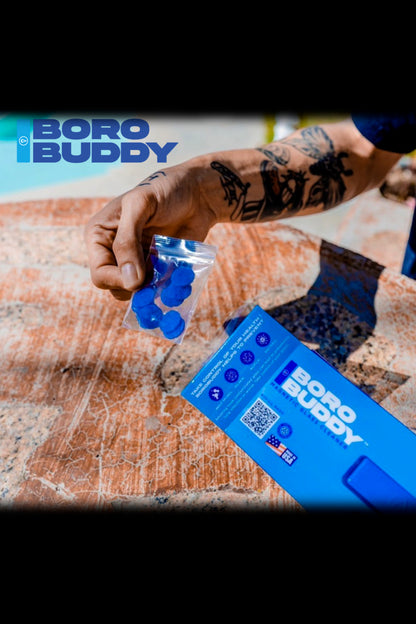 A person’s hand holds a package of blue cannabis rosin pods branded “Boro Buddy” against a textured blue surface.