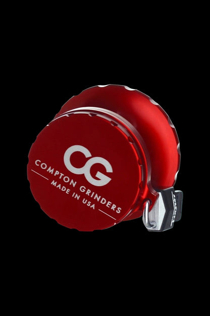 Red Compton Grinders cannabis grinder with white logo, isolated on black.
