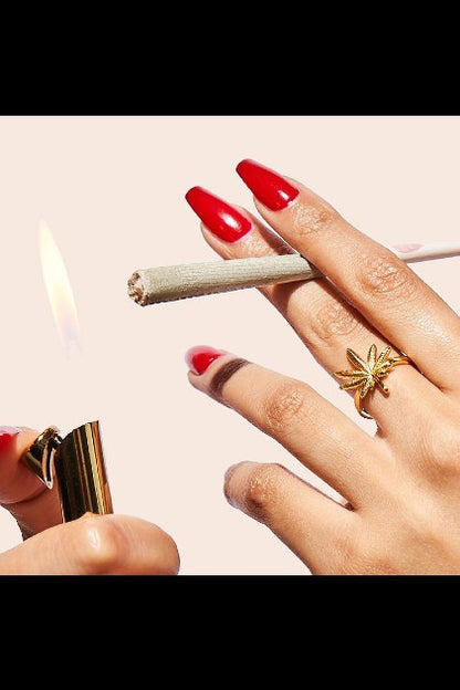 Close-up of manicured nails lighting a joint with a gold lighter.