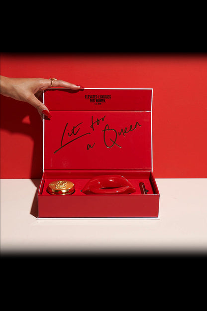 Red gift box with cannabis accessories and the handwritten message “Lit for a Queen” against a red background, with a hand reaching towards it.