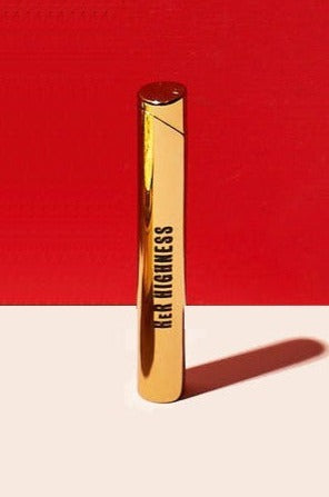 Gold cannabis vape pen with “Her Highness” text, casting a long shadow on a white surface against a red backdrop.