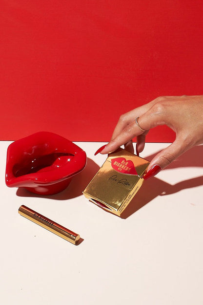 Golden cannabis vape pen packaging and a red ashtray on a vibrant red surface, hinting at a luxury cannabis experience.