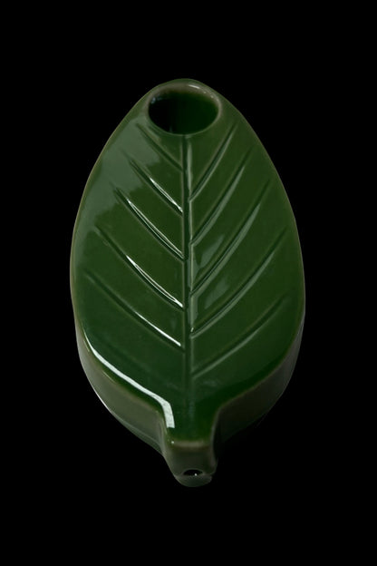 Green ceramic leaf-shaped pipe isolated on a black background.