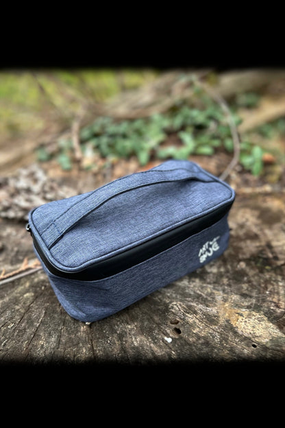 Blue cannabis accessories case with branded logo resting on a weathered wooden surface amidst foliage.