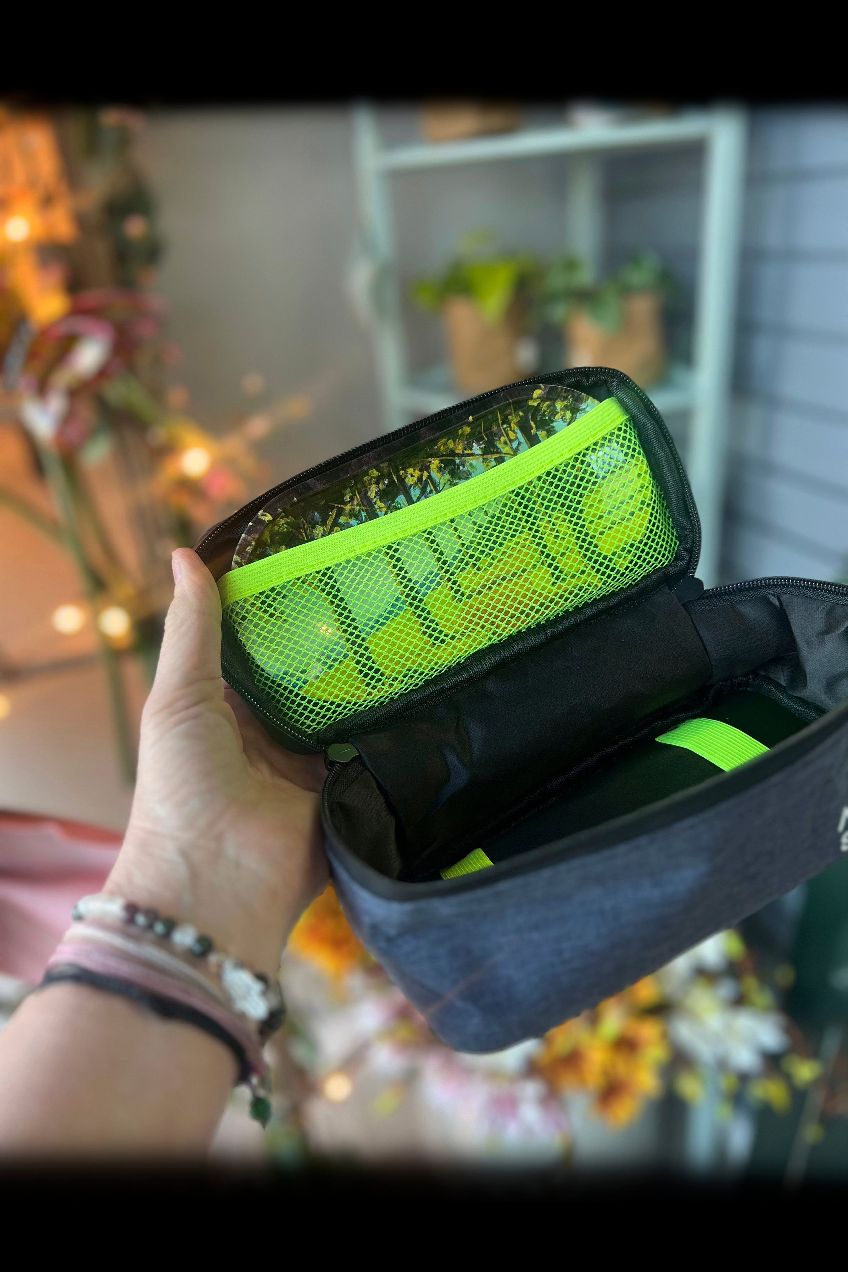 A hand holds open a smell-proof cannabis accessories case revealing bright green buds inside. <start_of_image>