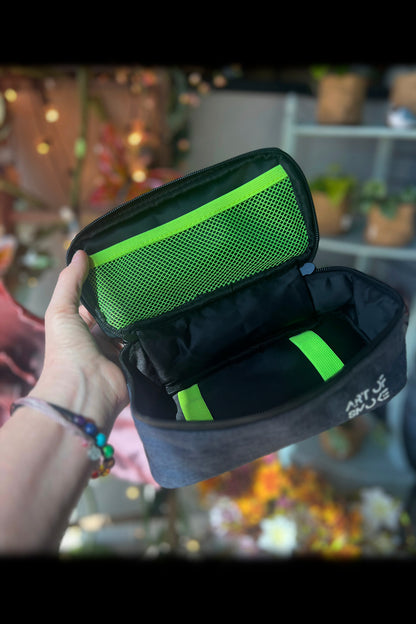 Open grey cannabis smell-proof bag with green accents and organization pockets, displayed in a dispensary setting.