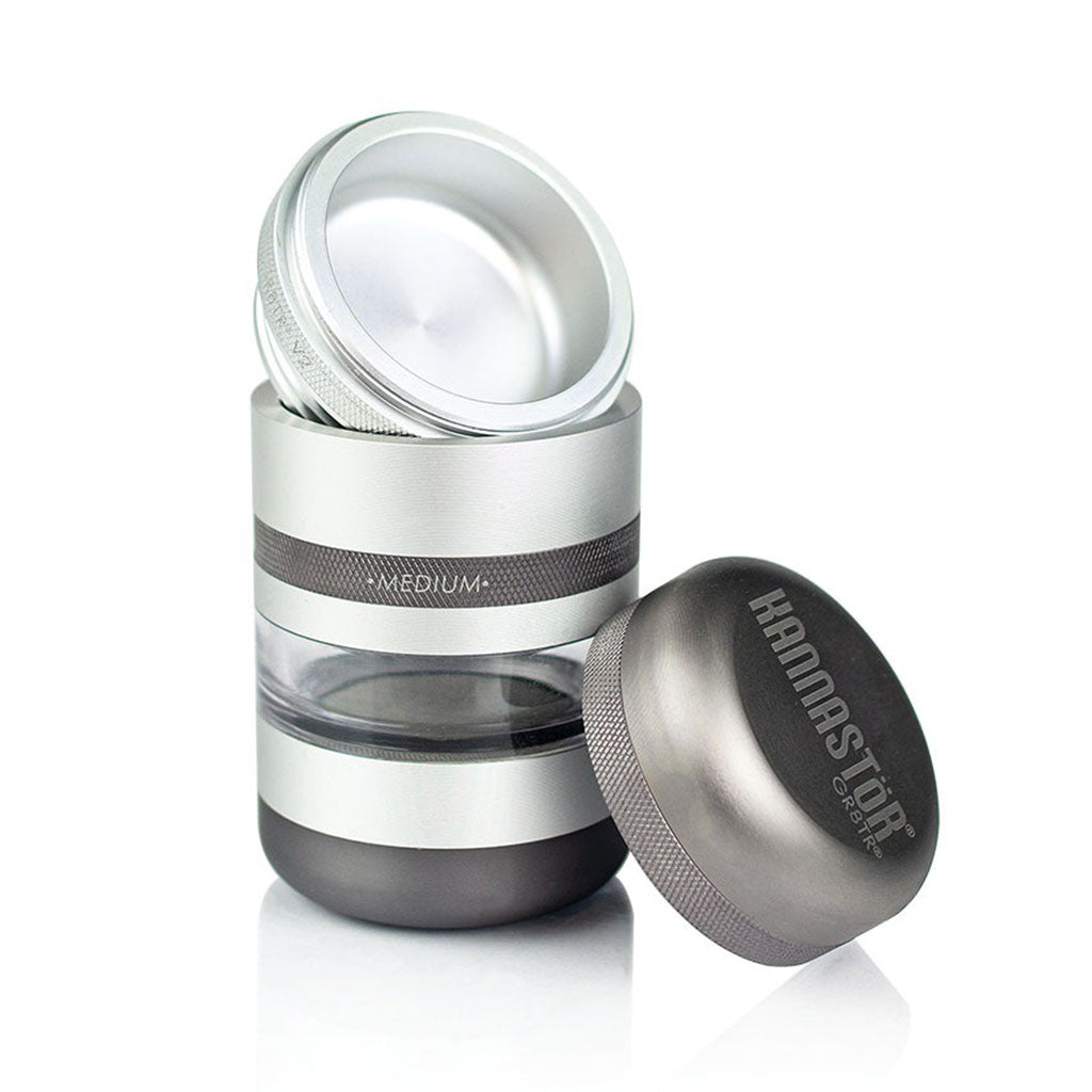 Three-quarter view of the silver RYOT GR8TR Jar Body Grinder with its lid removed and placed beside the clear midsection reflecting studio light.