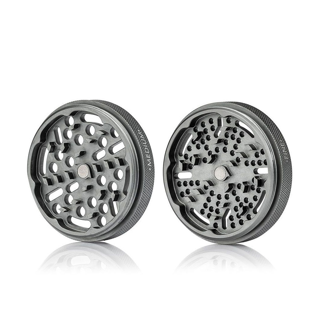 Two angled halves of the RYOT GR8TR Jar Body Grinder shown on a white background, revealing textured rims and staggered perforated grinding plates.
