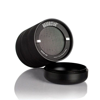 Angled close-up of the black RYOT GR8TR Jar Body Grinder showing its mesh screen, textured sides, and detached base on a reflective white surface.