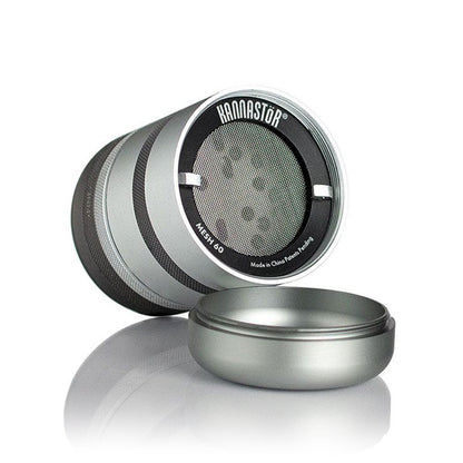Angled close-up of the silver RYOT GR8TR Jar Body Grinder showing its mesh screen and detached lid on a reflective surface.