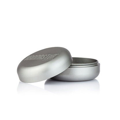 Low-angle studio shot of a silver RYOT GR8TR Jar Body Grinder with its lid propped beside the open base on a white reflective surface