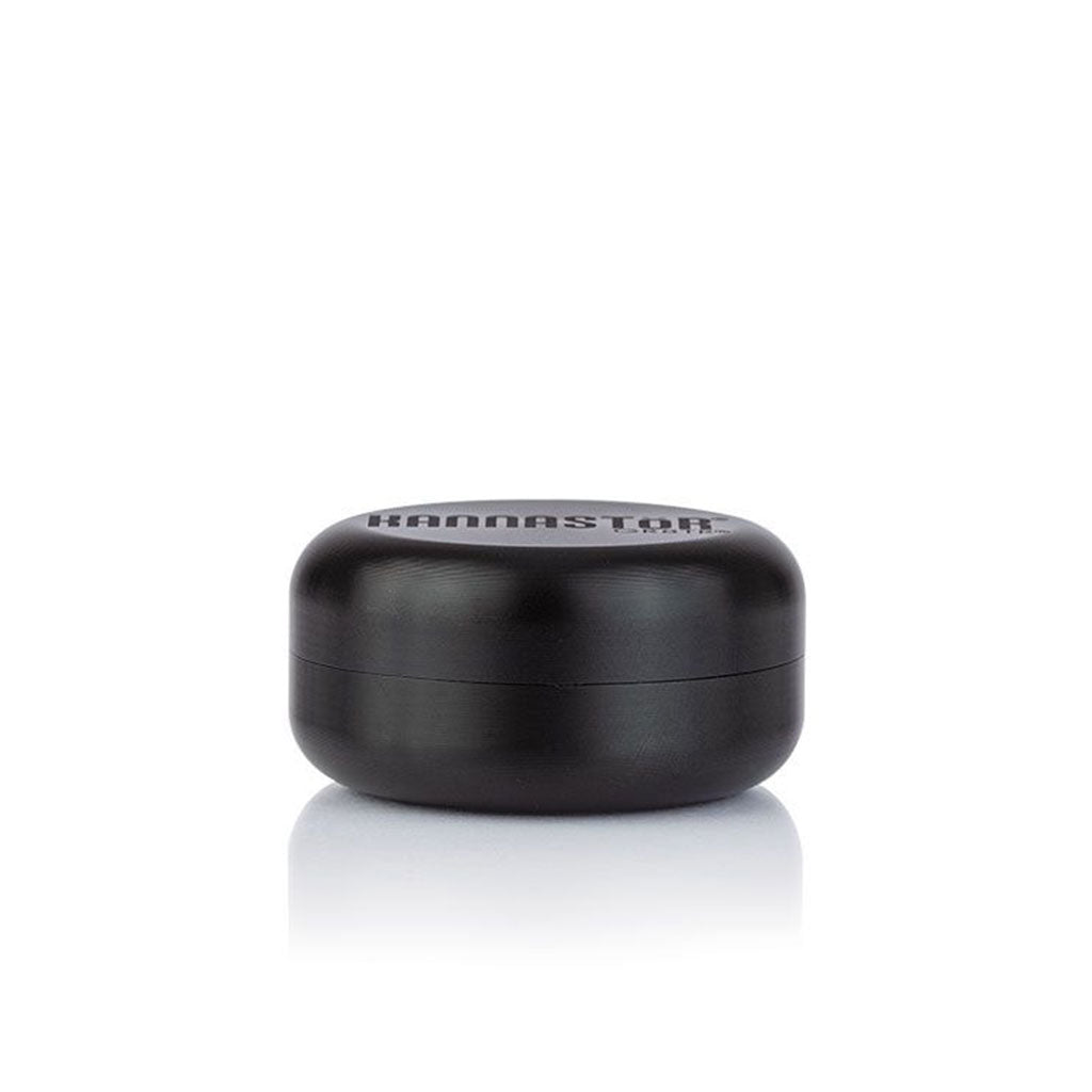 Front-facing shot of the black RYOT GR8TR Jar Body Grinder resting on a reflective white surface with soft studio lighting.