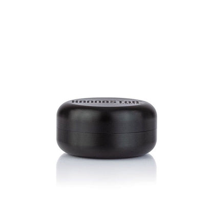 Front-facing shot of the black RYOT GR8TR Jar Body Grinder resting on a reflective white surface with soft studio lighting.
