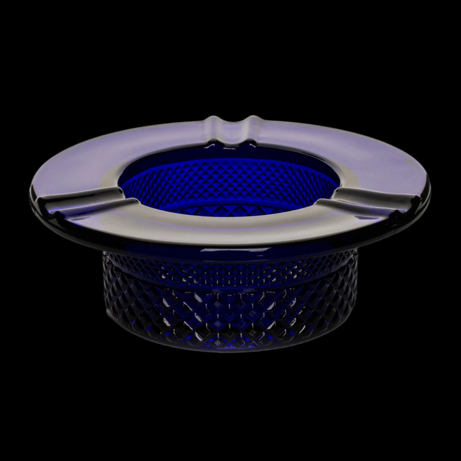 Blue glass ashtray with three indentations, isolated on a black background.