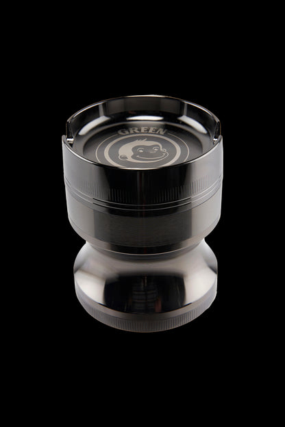 Close-up top-down view of the Green Monkey Chacma Grinder with Ashtray showing the shiny black metal finish and engraved monkey logo.