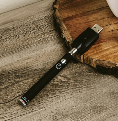 Black cannabis vape pen resting on a wood slice with a blurred background.