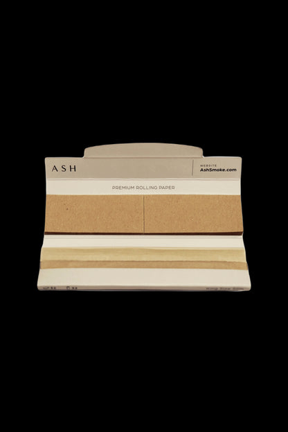Pack of beige rolling papers with “ASH” branding and website address on a white background.