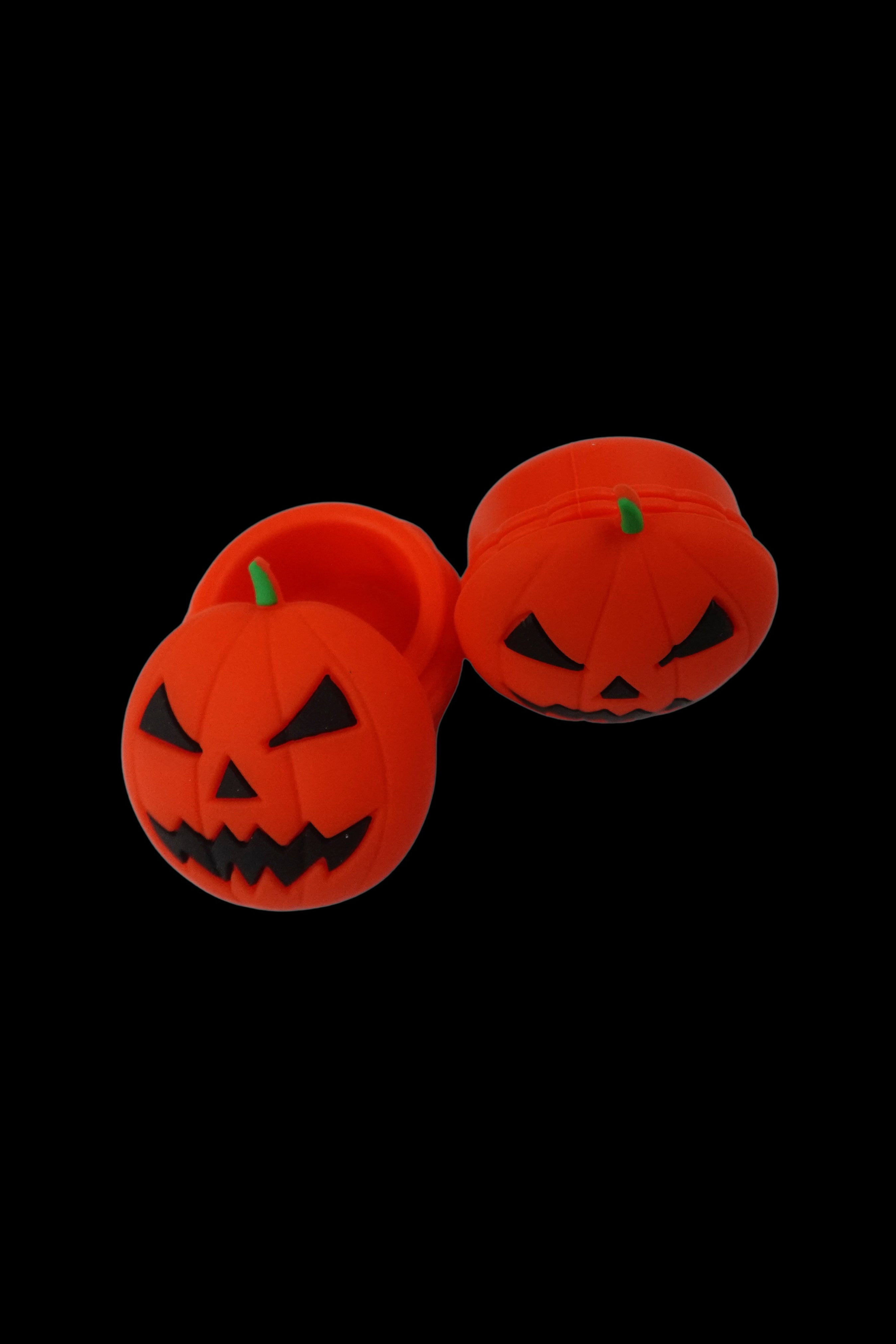 Two orange jack-o'-lantern-shaped silicone stash containers with green stems float against a black background.