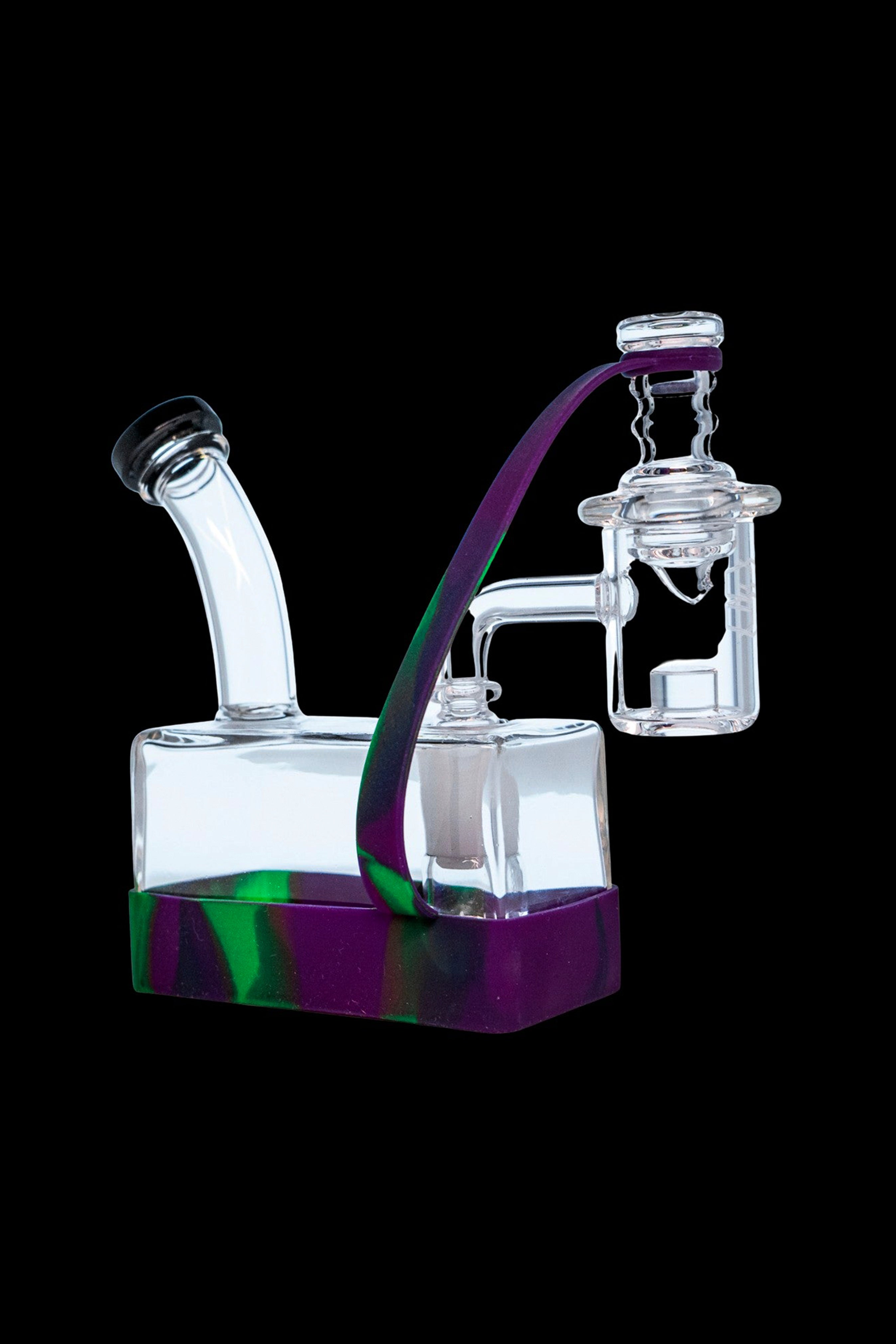A clear glass dab rig with purple and green accents, featuring a bubbler base and angled mouthpiece.