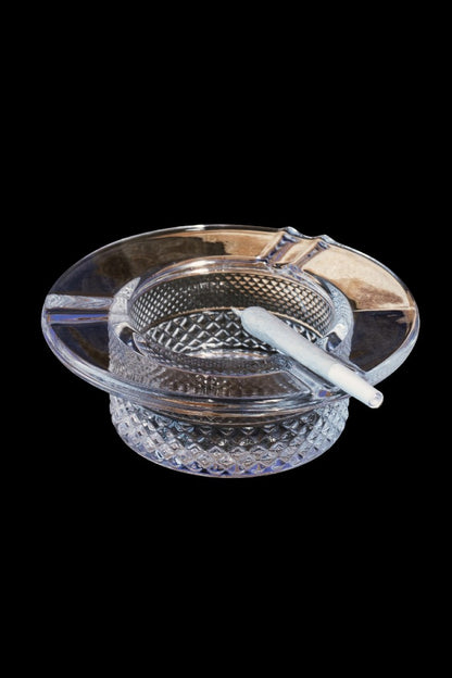 A clear glass ashtray with a partially smoked joint resting inside, set against a black background.