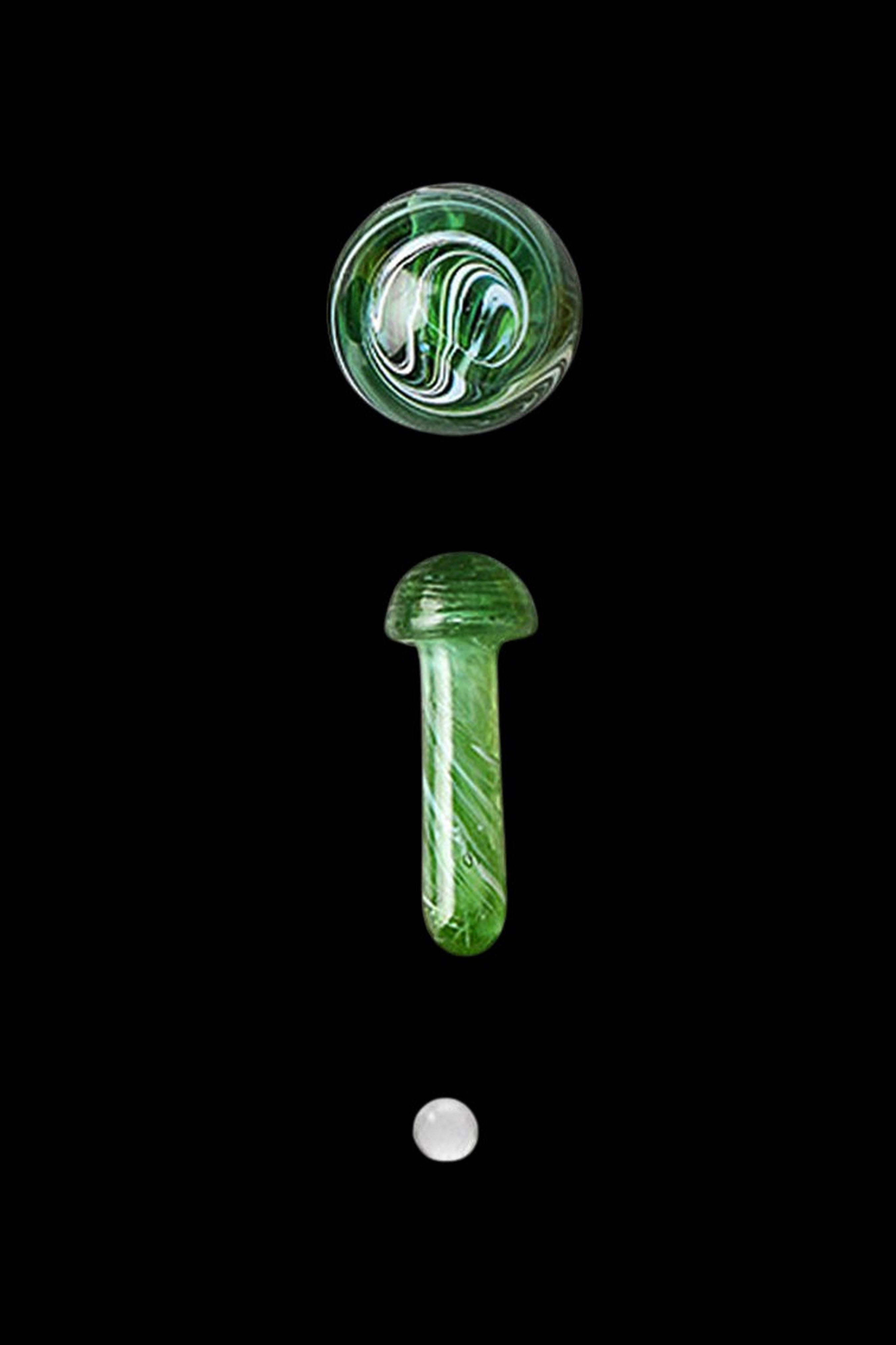 Green glass cannabis accessories including a marble, oil dome, and dab tool, isolated on a black background.