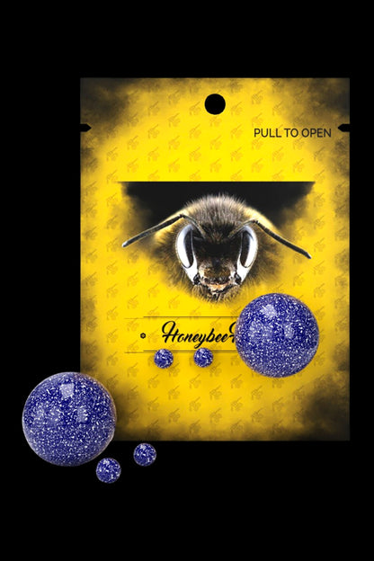 Yellow cannabis packaging with a bee illustration and three dark blue, glittery hash rosin balls.