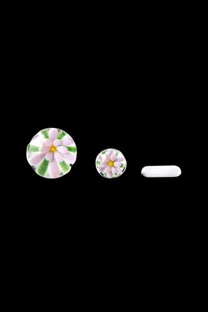 Hand-blown glass cannabis accessories featuring floral designs, including a cap, insert, and tip, against a black background.