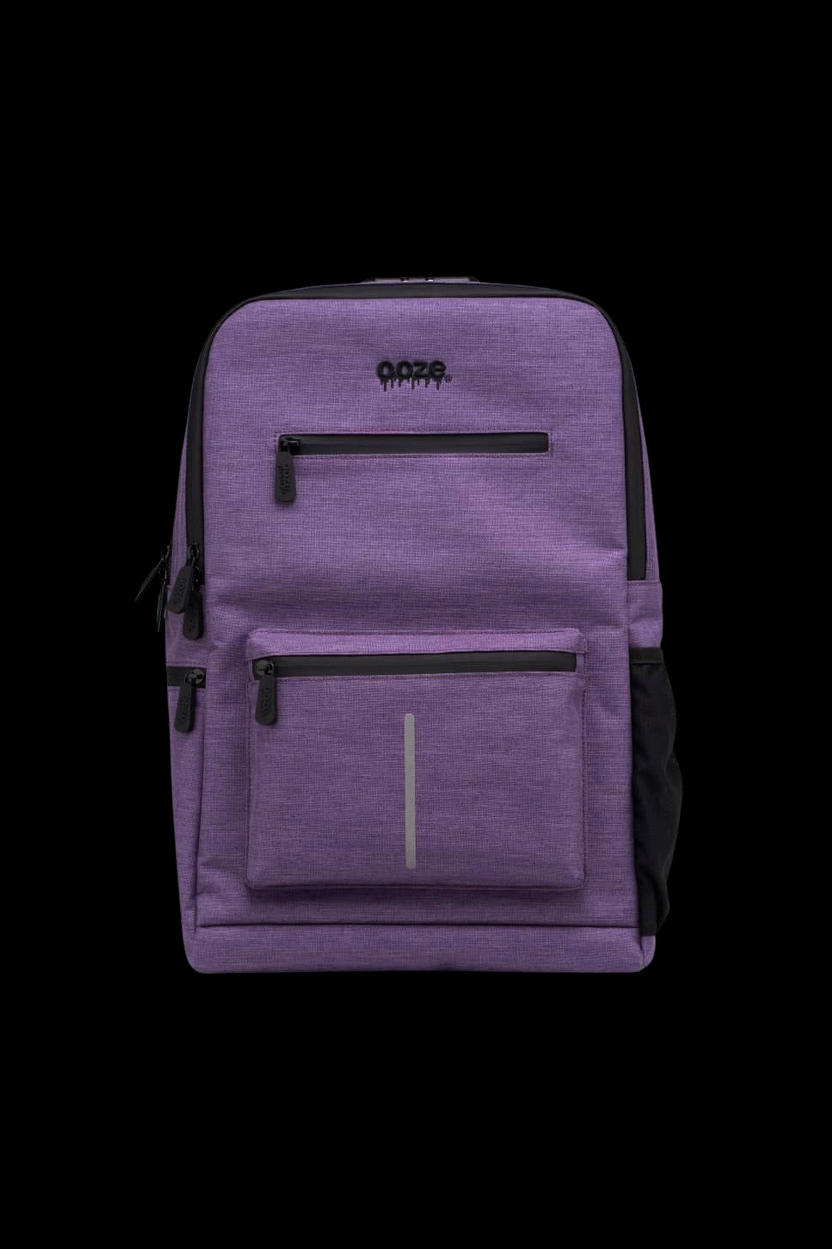 Close-up front view of the purple Ooze Traveler Smell Proof Backpack showing top and front zip pockets, reflective strip and black zipper accents