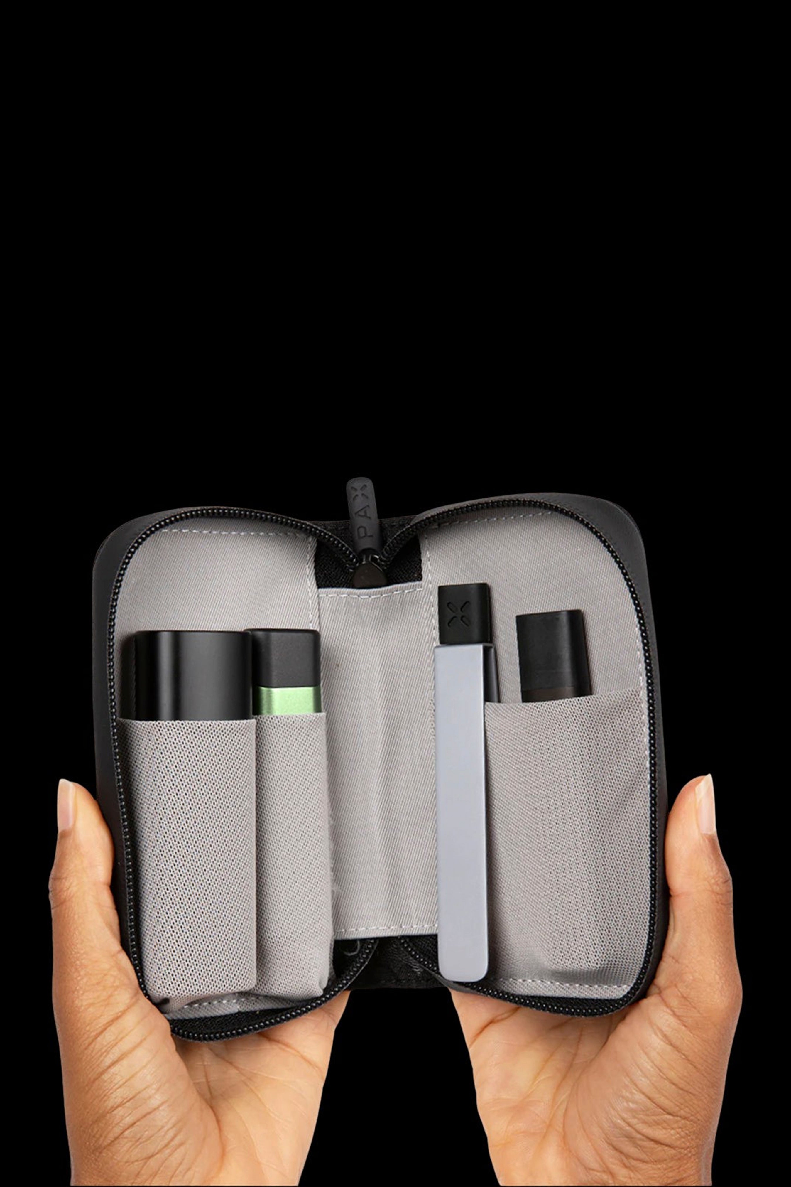 Hands holding open a black cannabis accessory case containing a vaporizer pen and other components on gray foam.