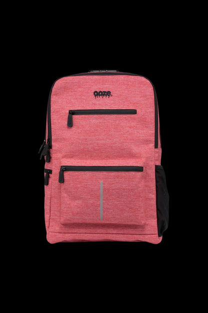 Close-up front view of a coral red Ooze Traveler Smell Proof Backpack against a black background, showing two zippered pockets and the logo.